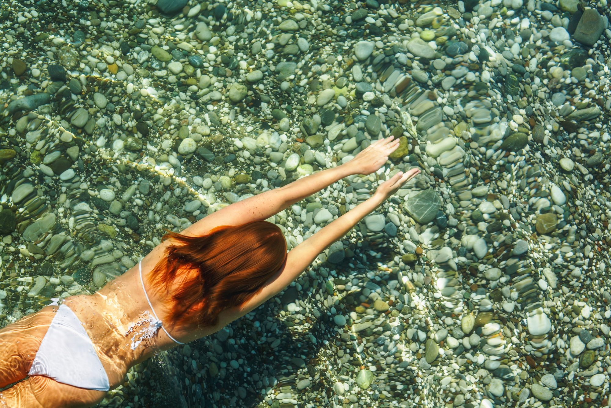 frau-taucht-in-gruenem-wasser-steine-am-grund