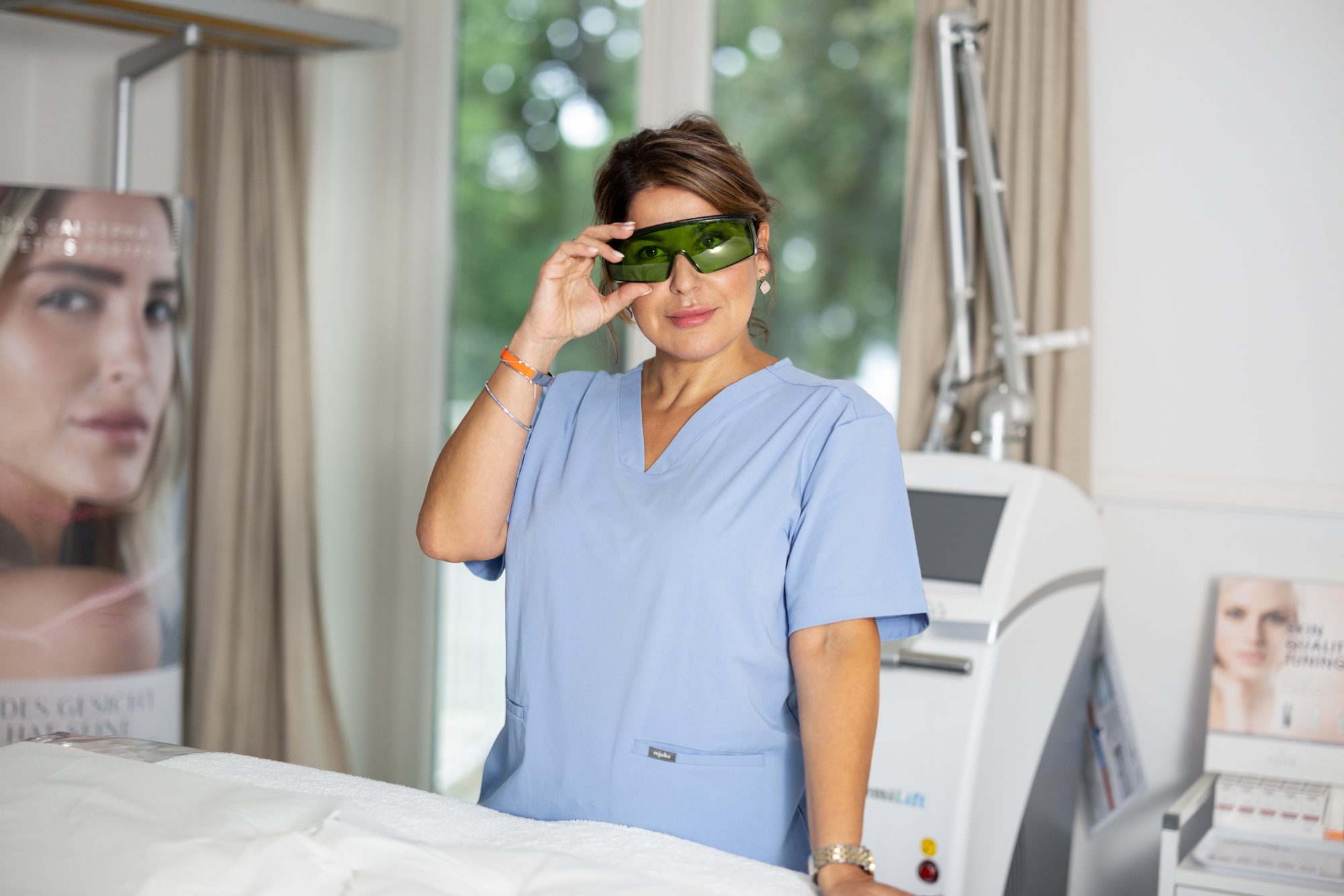 Frau in blauer Kleidung mit grüner Schutzbrille neben einem Gerät.