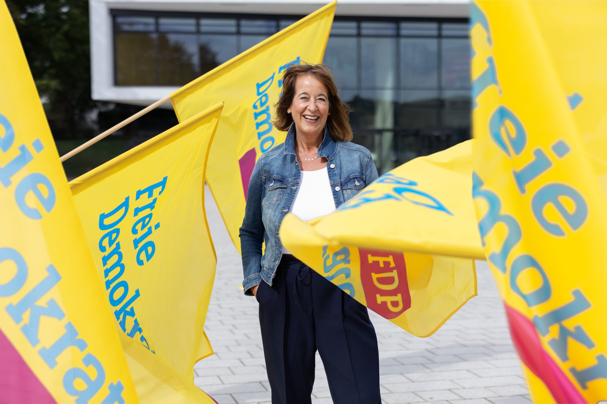 Frau in einer Jeansjacke zwischen gelben Fahnen der Freien Demokraten.
