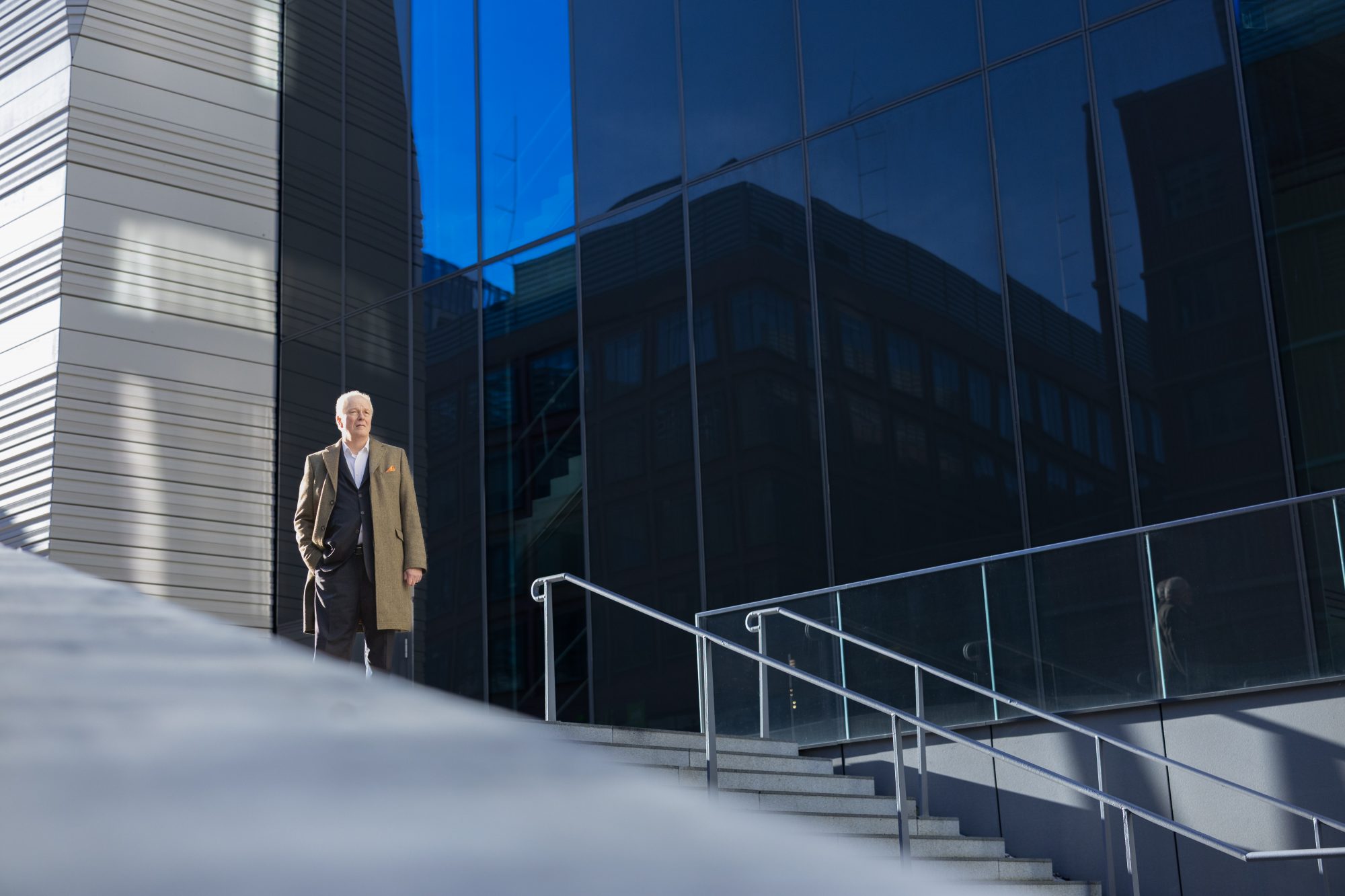Henning von Gersdorff steht neben einer breiten Treppe vor einem verglasten Gebäude.