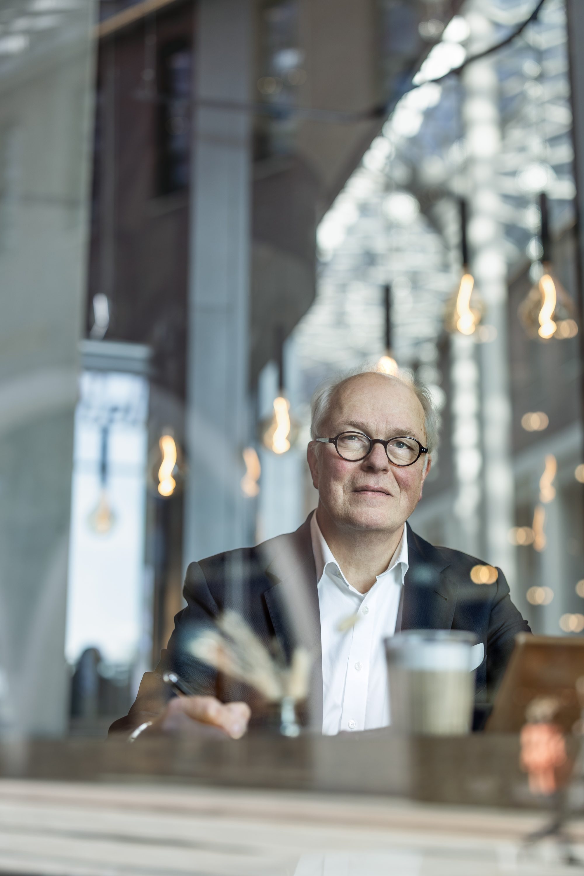 Henning von Gersdorff sitzt mit einer Tasse hinter der Fensterscheibe eines Cafés.