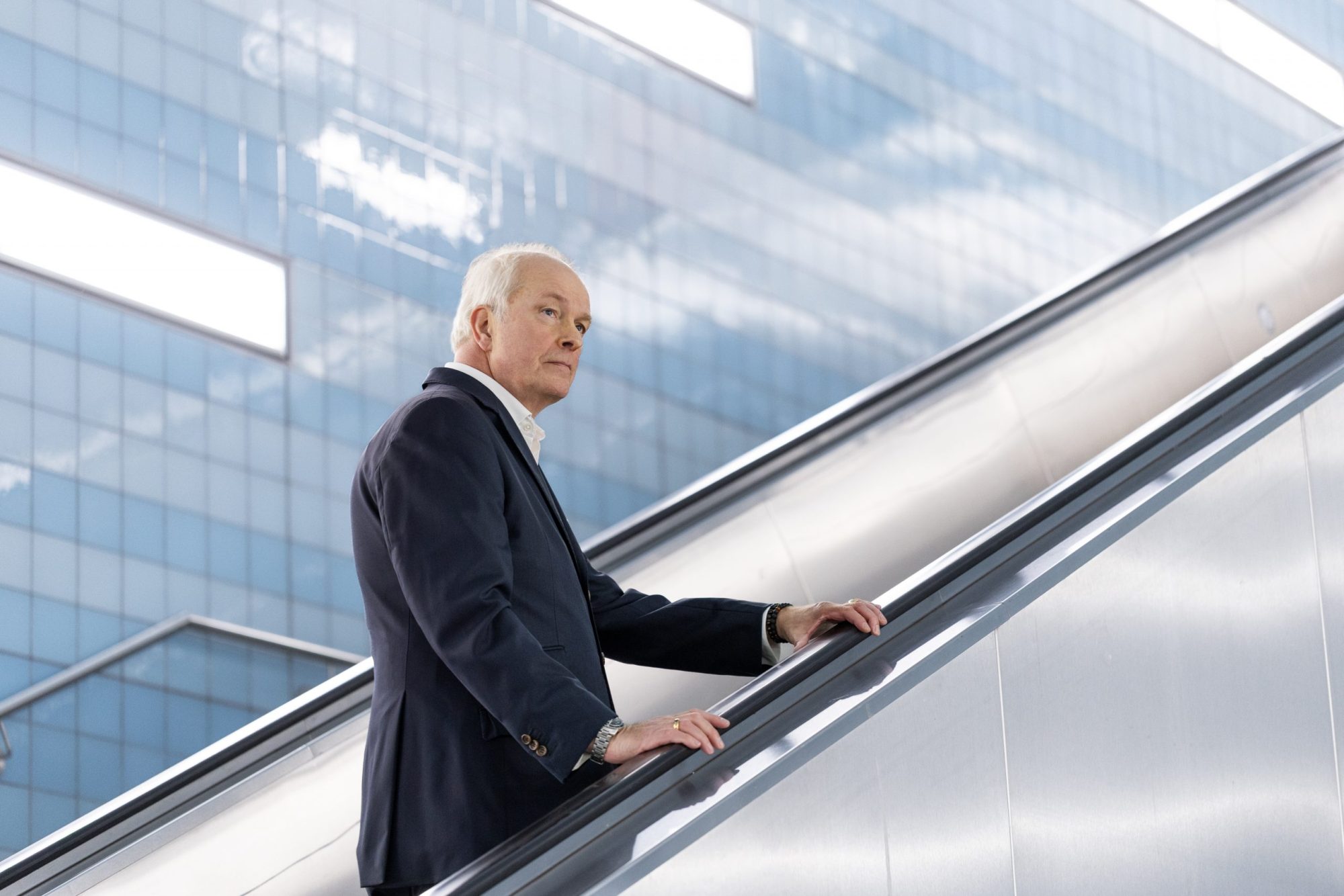 Henning von Gersdorff fährt mit einer Rolltreppe durch ein modernes Gebäude.