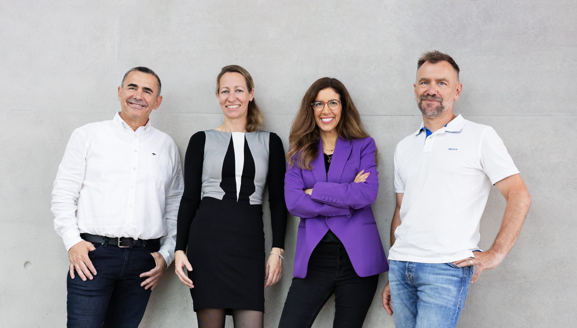 Vier Mitglieder von Bündnis Technik stehen lächelnd in einer Reihe vor einer hellen Wand.