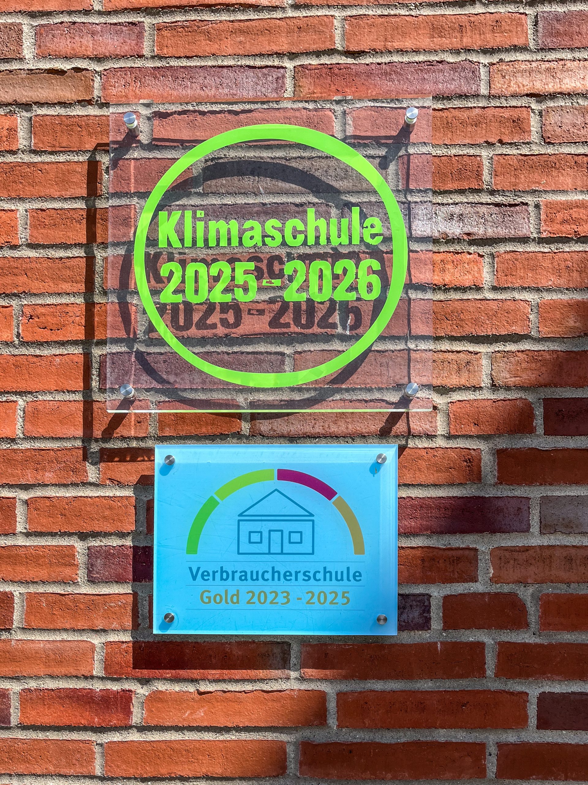 Schilder für Klimaschule und Verbraucherschule an einer Backsteinwand.