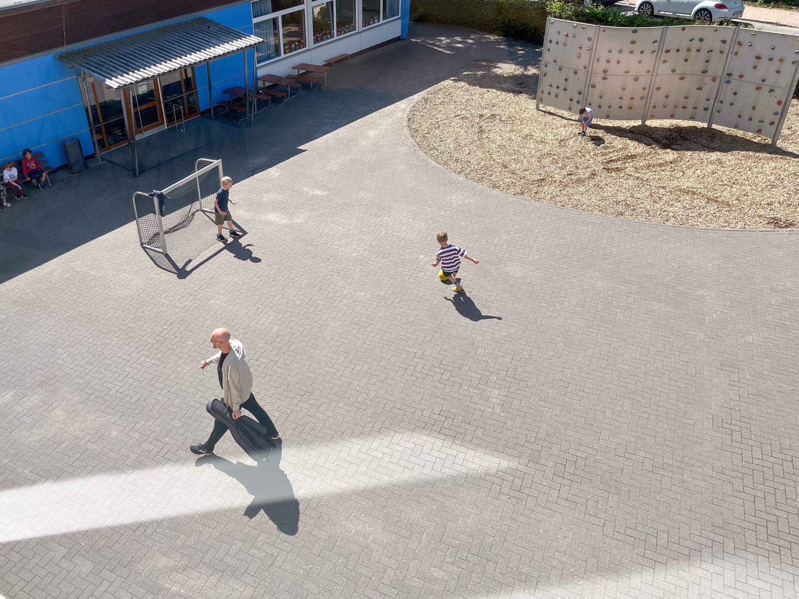 Blick von oben auf Kinder, Basketballkorb und Kletterwand auf dem Schulhof.