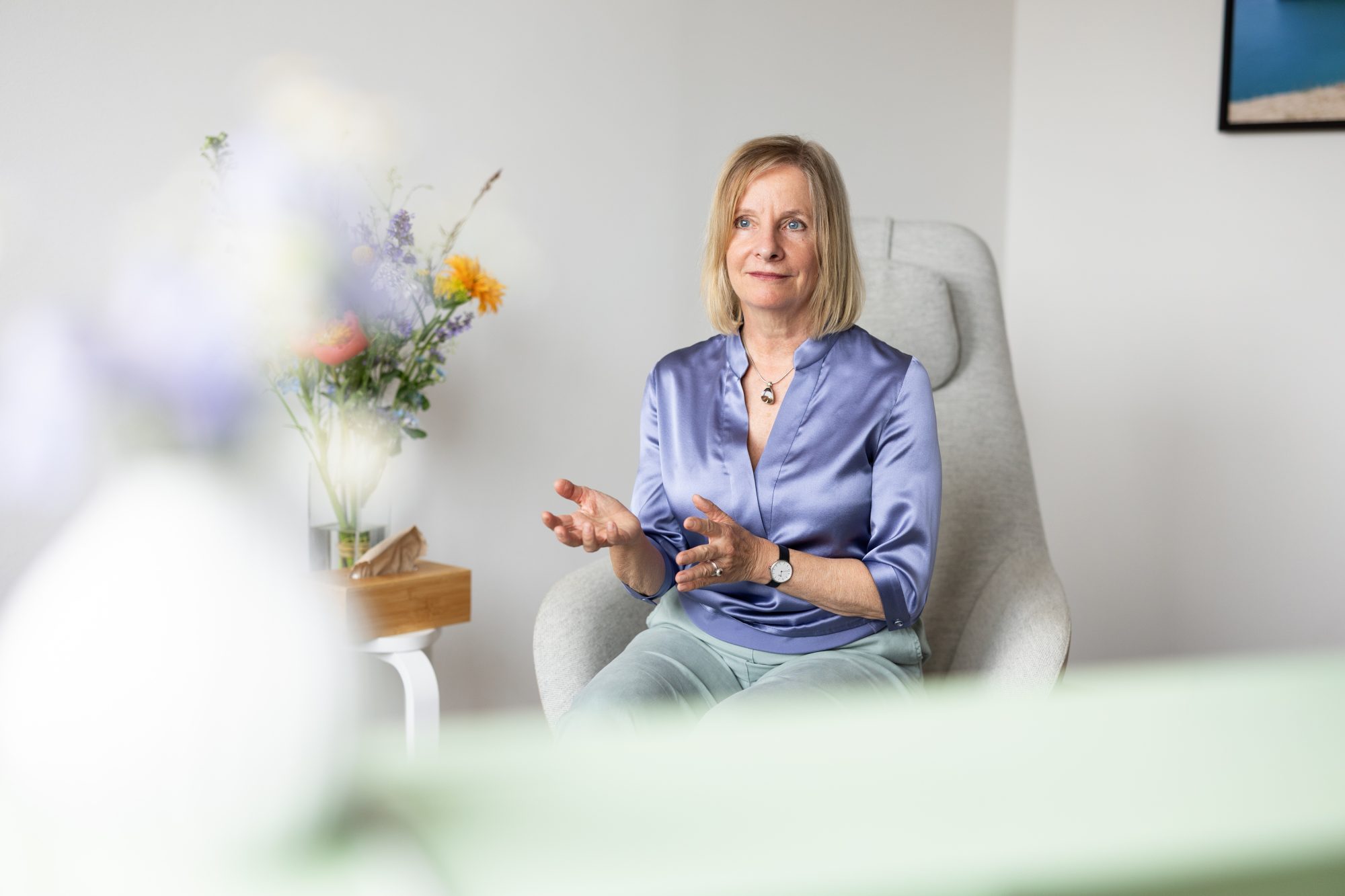 Nanette Toillié gestikuliert im Gespräch, im Vordergrund stehen unscharfe Blumen.