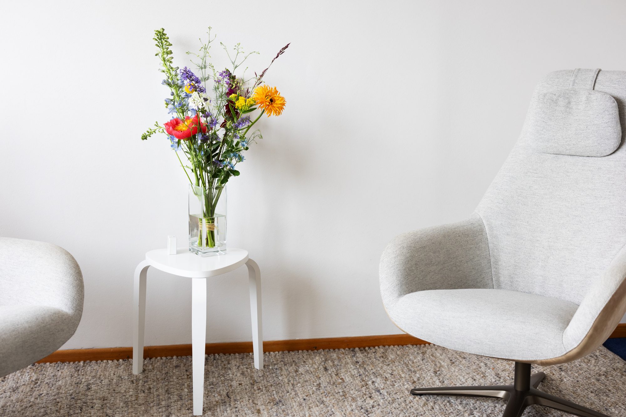 Bunter Blumenstrauß auf einem kleinen weißen Tisch zwischen zwei hellen Sesseln.