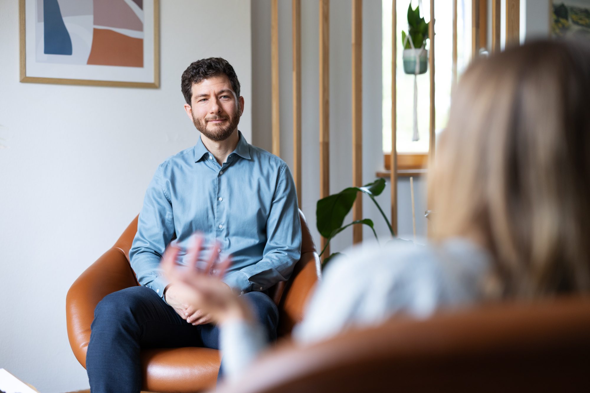 Bertram Schenkluhn lächelt seiner Gesprächspartnerin gegenüber in einem orangefarbenen Sessel.