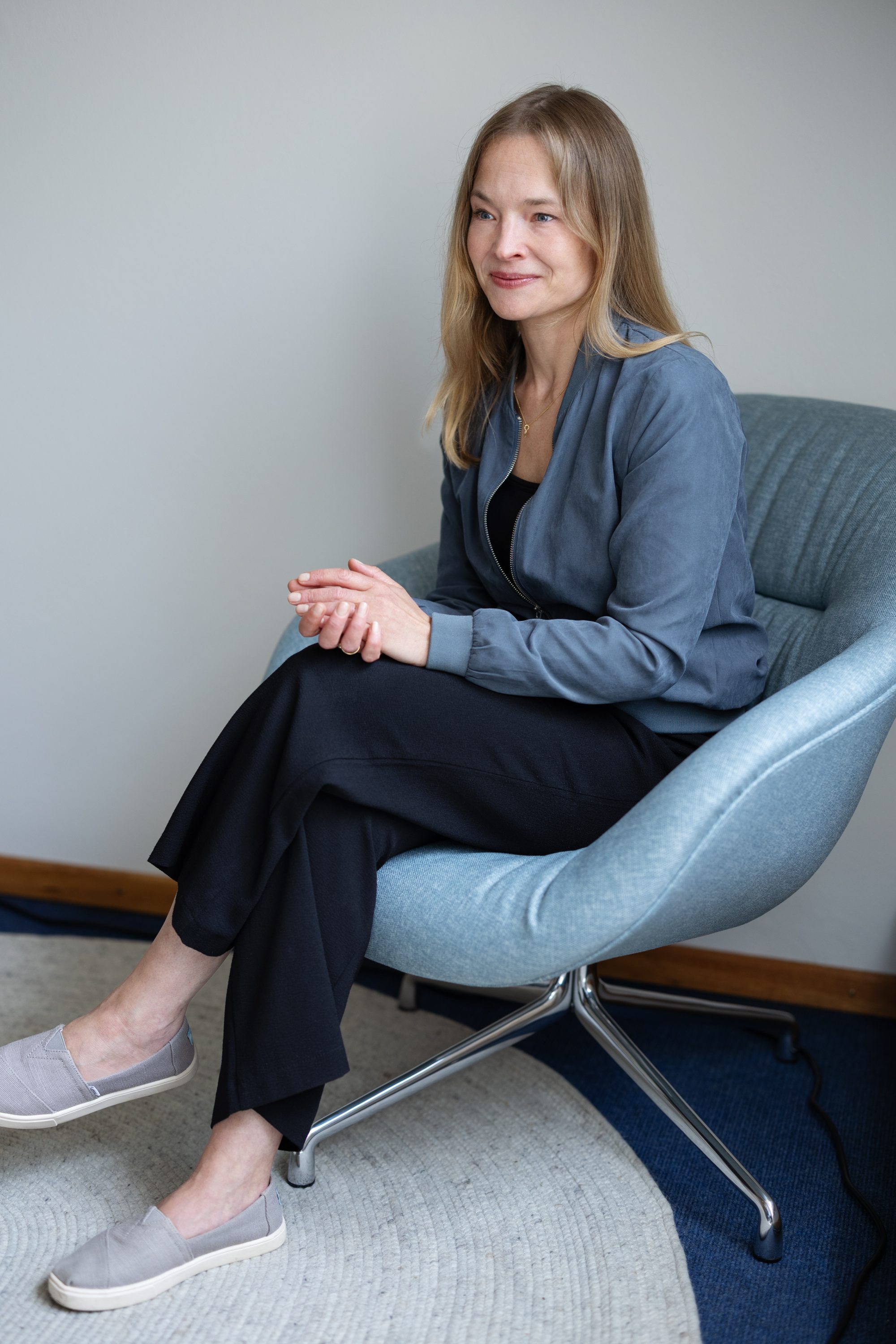 Christiane Simon sitzt in einem hellblauen Sessel neben einer weißen Wand.