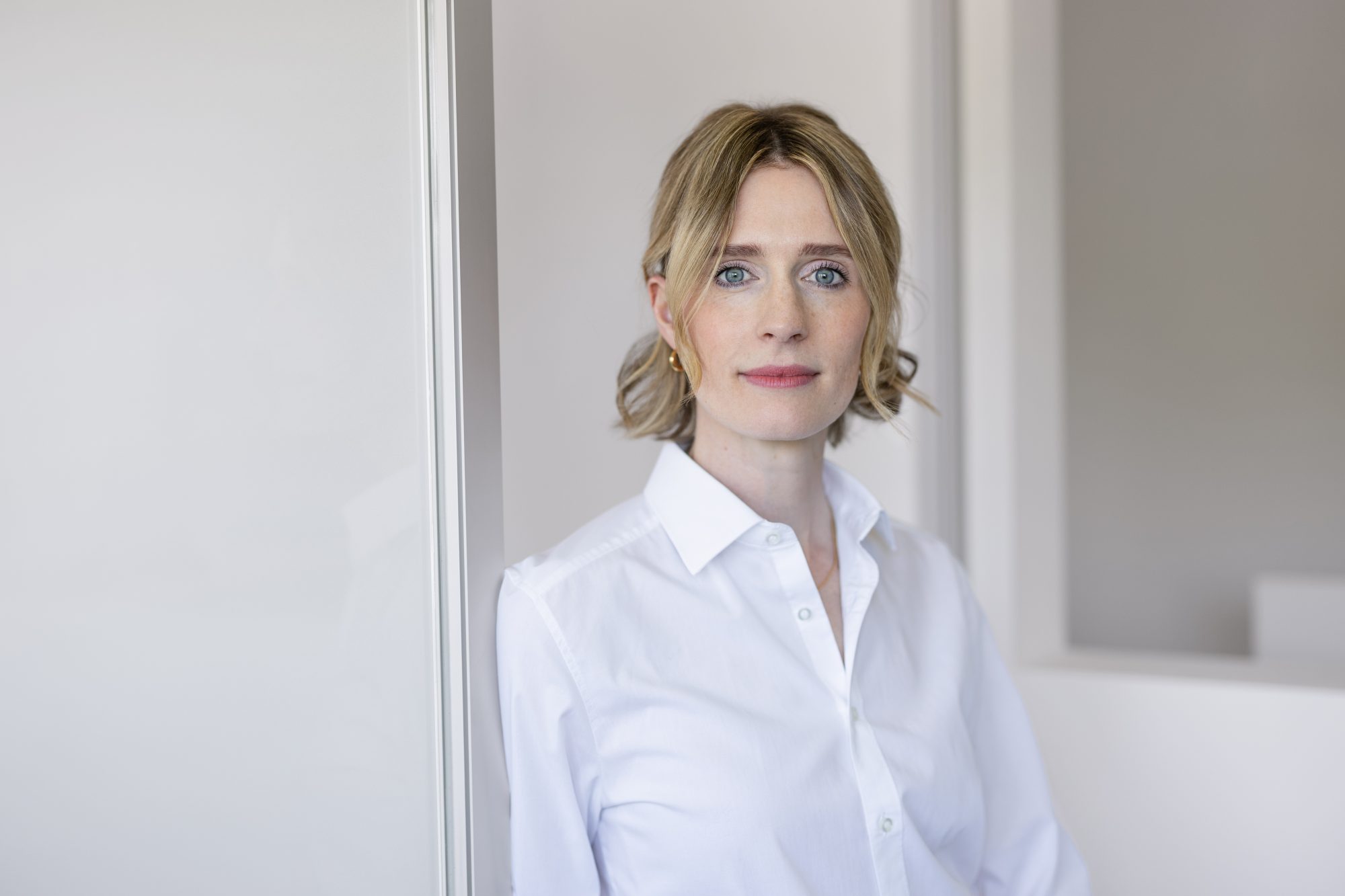Porträt einer Frau in weißer Bluse vor einer hellen Wand in der Praxis.
