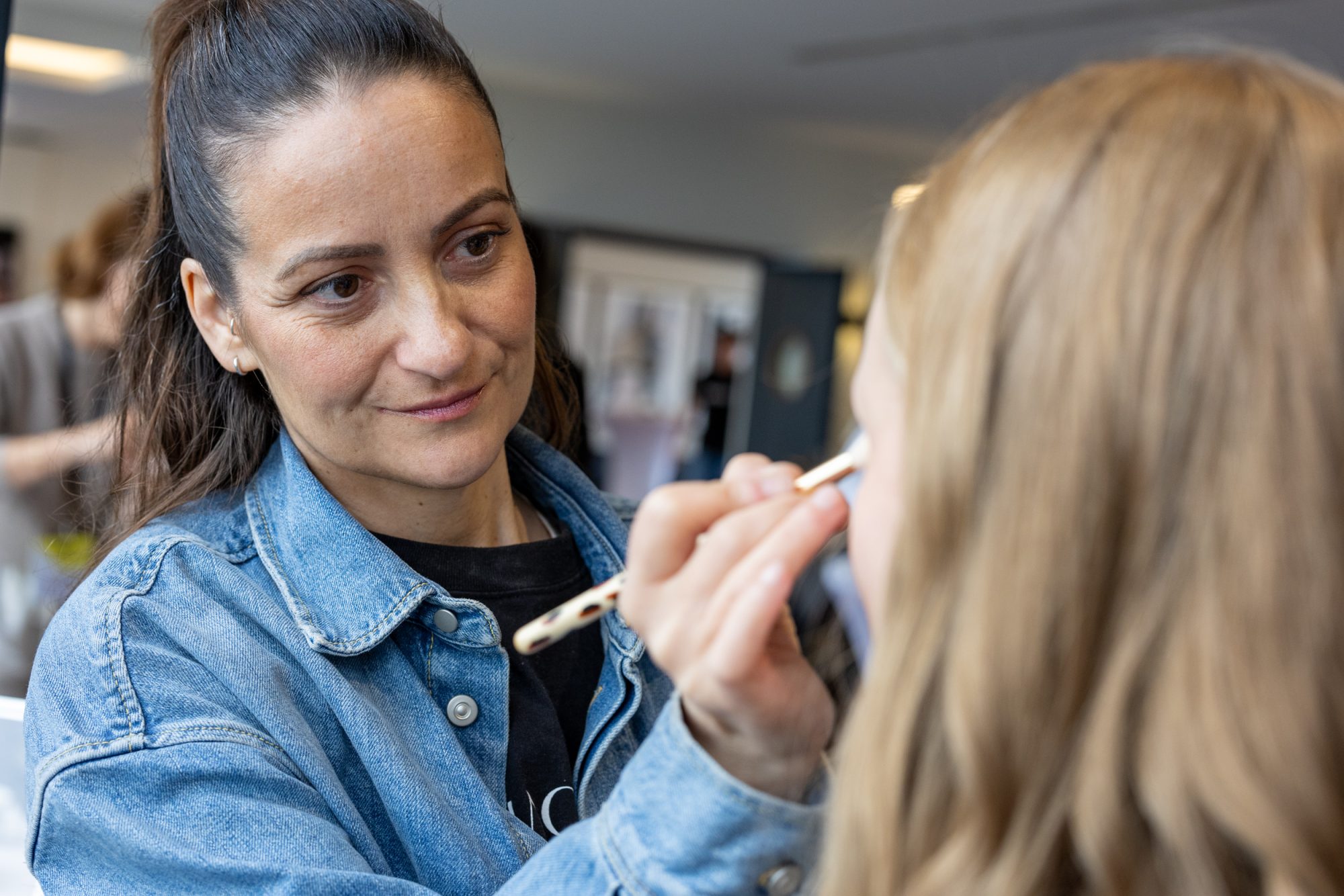 Eine Frau trägt einer Besucherin mit einem Pinsel Make-up auf.