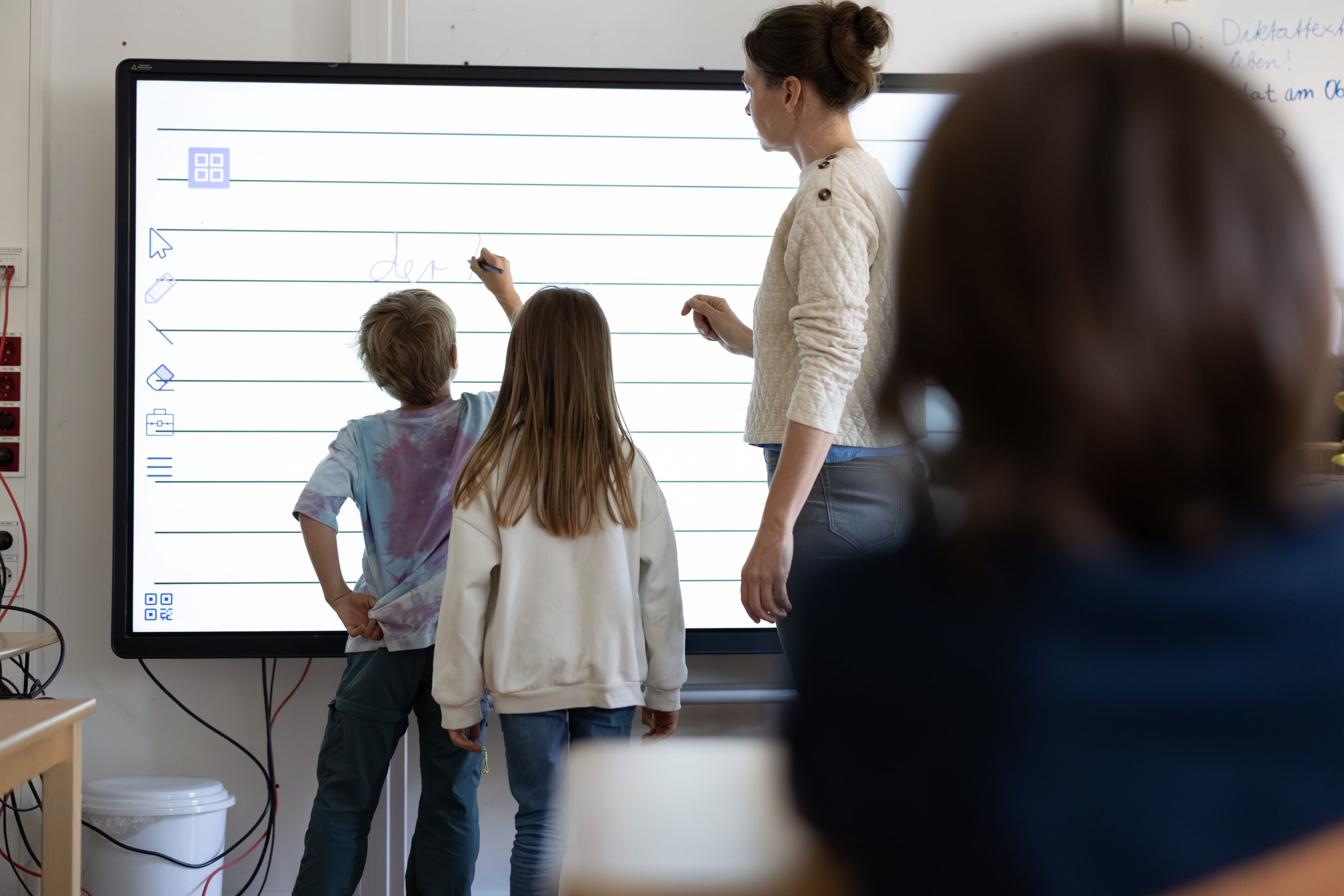 Kinder und eine Lehrkraft arbeiten an einer digitalen Tafel mit Notenlinien.