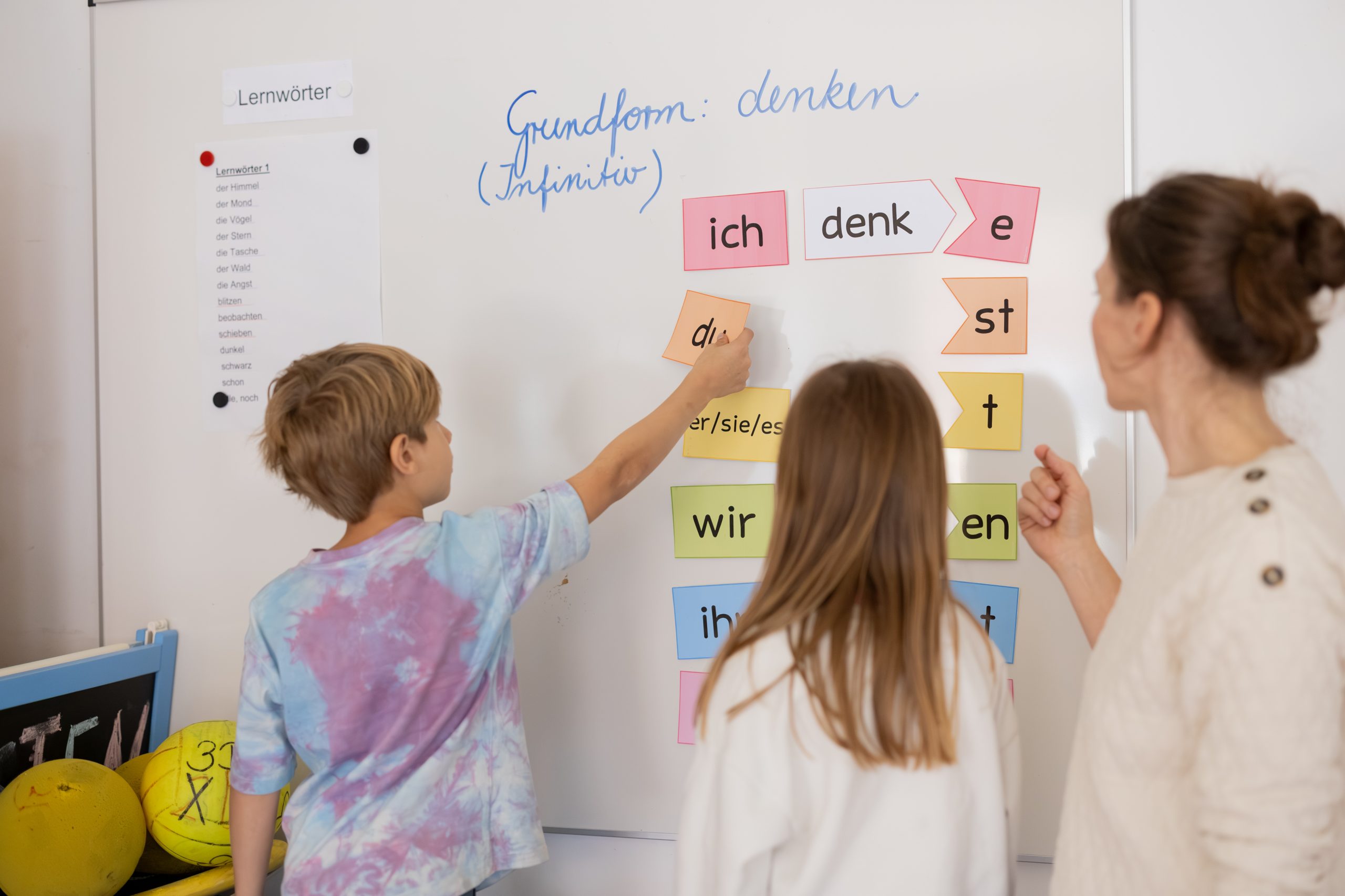 Kinder ordnen Wortkarten an einer Tafel, begleitet von einer Lehrkraft.