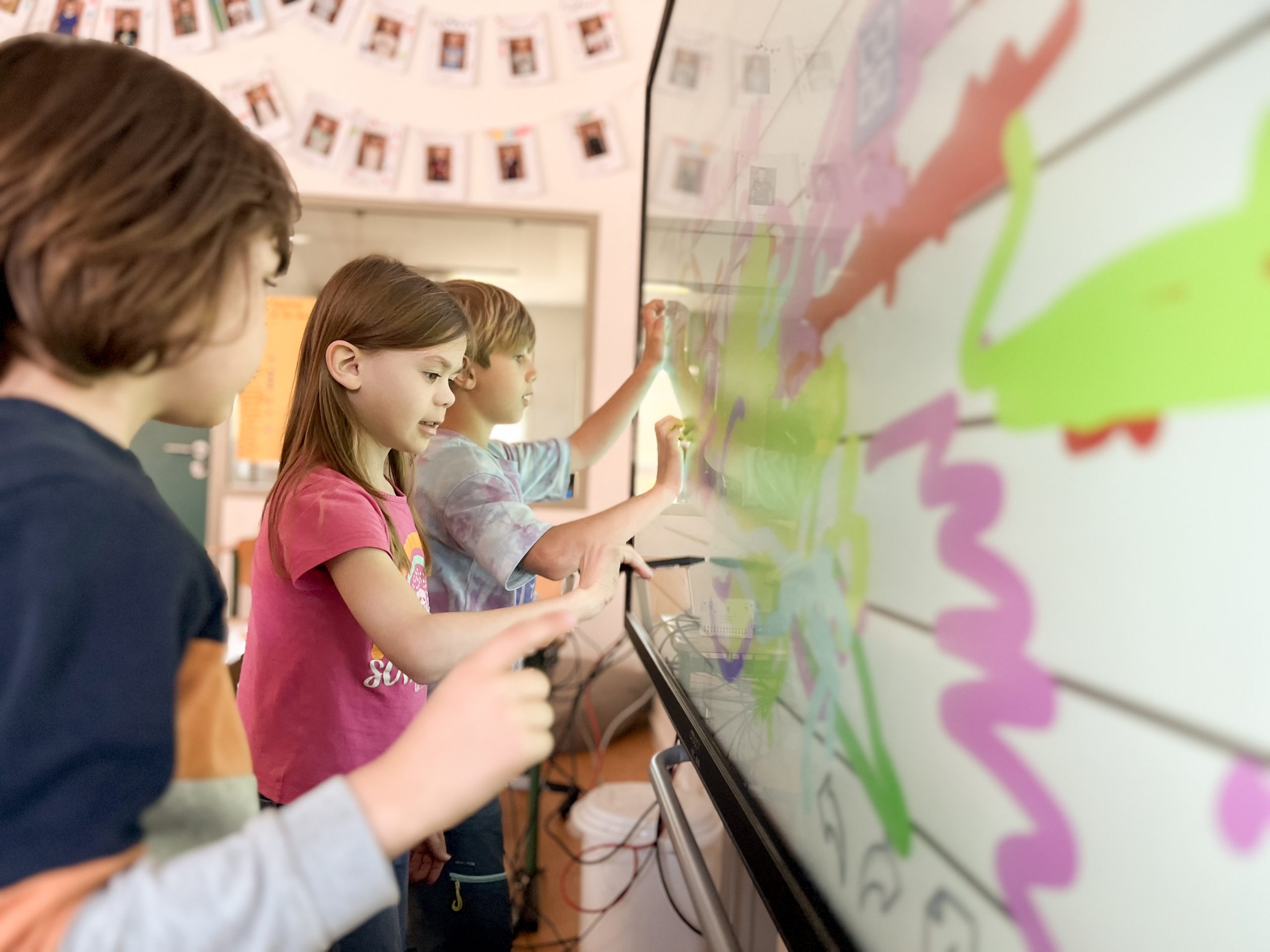 Kinder gestalten ein farbiges Bild an einer digitalen Tafel.